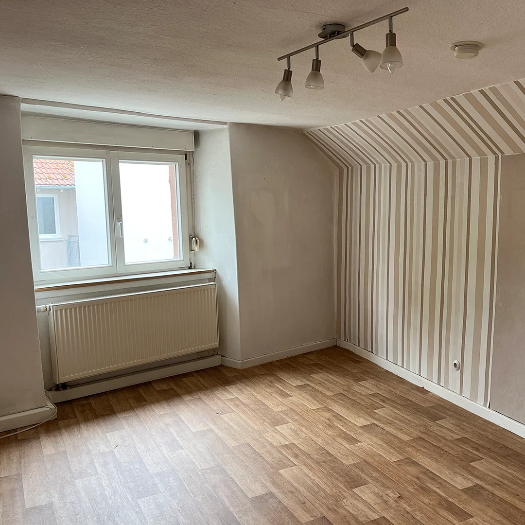 Einfamilienhaus Appenheim Hintergasse Schlafzimmer Leeres Schlafzimmer mit schräger Wand, gestreifter Tapete, Fenster und Heizkörper unter der Fensterbank.