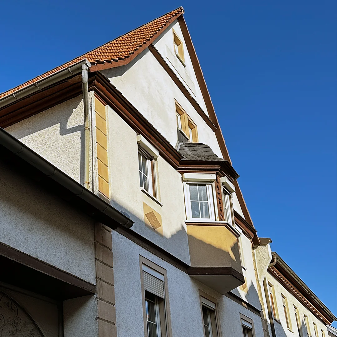 Einfamilienhaus Essenheim Hauptstraße Außenansicht 2 Gebäude mit hell verputzter Fassade, geneigtem Ziegeldach, vorspringendem Erker, mehreren Fenstern, Dachüberstand, Regenrinne und gleichmäßiger Tageslichtbeleuchtung.