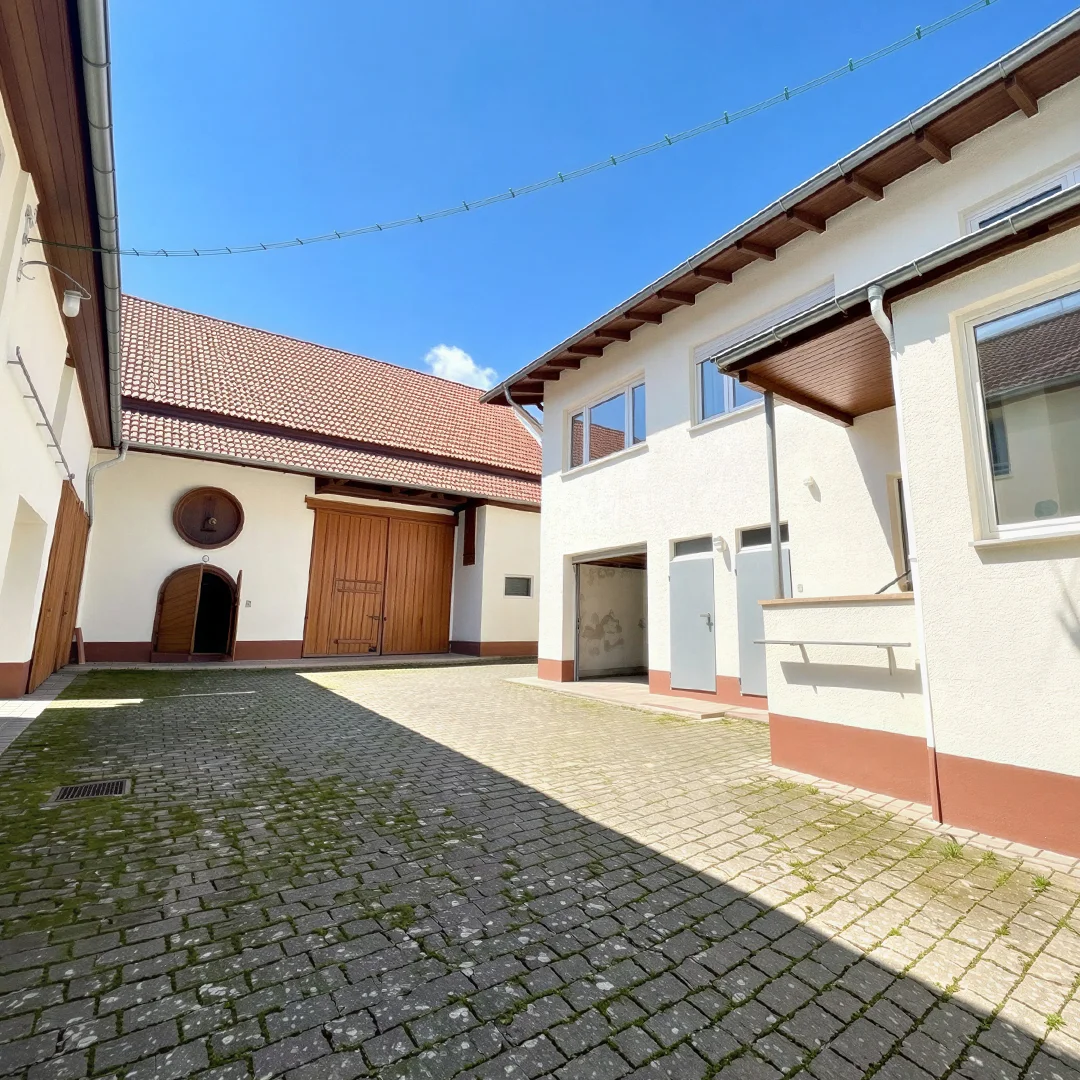 Innenhof eines Einfamilienhauses mit gepflastertem Boden, weißen Fassaden und braunen Dächern unter blauem Himmel