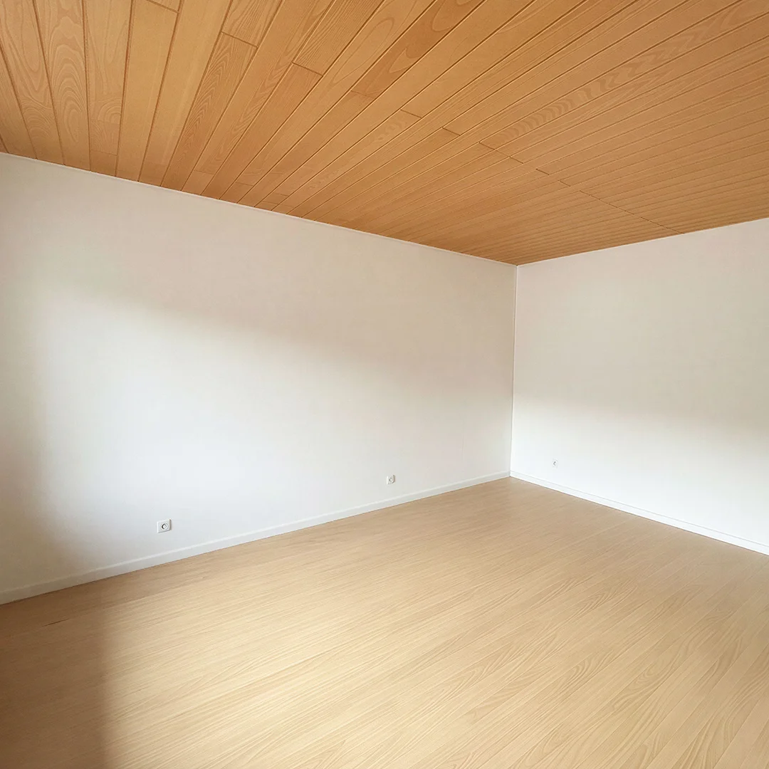 Leerer Raum mit hellen Holzboden und weiß gestrichenen Wänden unter einer Holzdecke