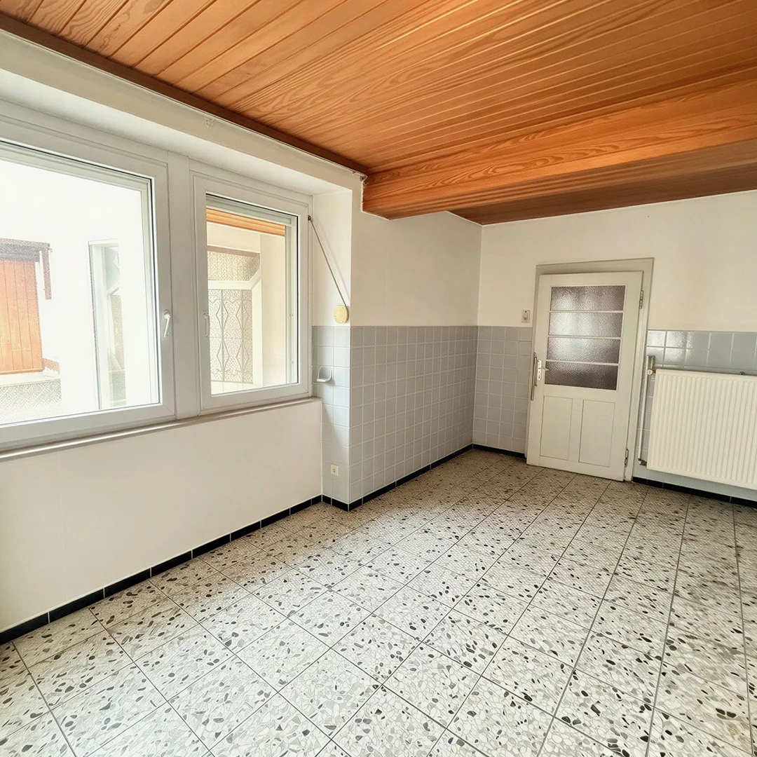 Leerer Raum mit gefliestem Boden, halbhohen Wandfliesen, Holzdecke, Fenster und Tür mit Milchglasscheiben
