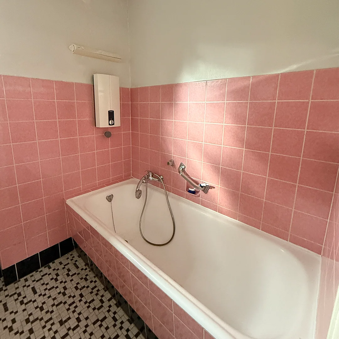 Badezimmer mit Badewanne, rosa Wandfliesen und schwarz-weiß gemustertem Boden.