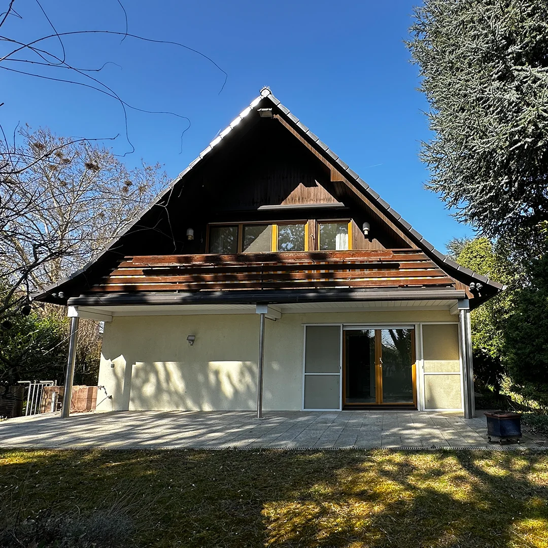 Einfamilienhaus Mainz Schulrat Spang Straße Außenansicht Holzhaus mit geneigtem Dach, Balkon, großflächiger Terrasse, Fenster- und Türelementen sowie umliegender Grünfläche bei natürlichem Tageslicht.
