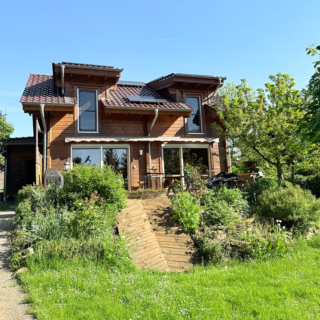 Holzhaus Mainz-Marienborn An der Kirschhecke Außenansicht eines Holzhauses mit holzverkleideter Fassade, geneigtem Dach, Terrassenbereich, Gartenanlage und natürlichem Tageslicht.