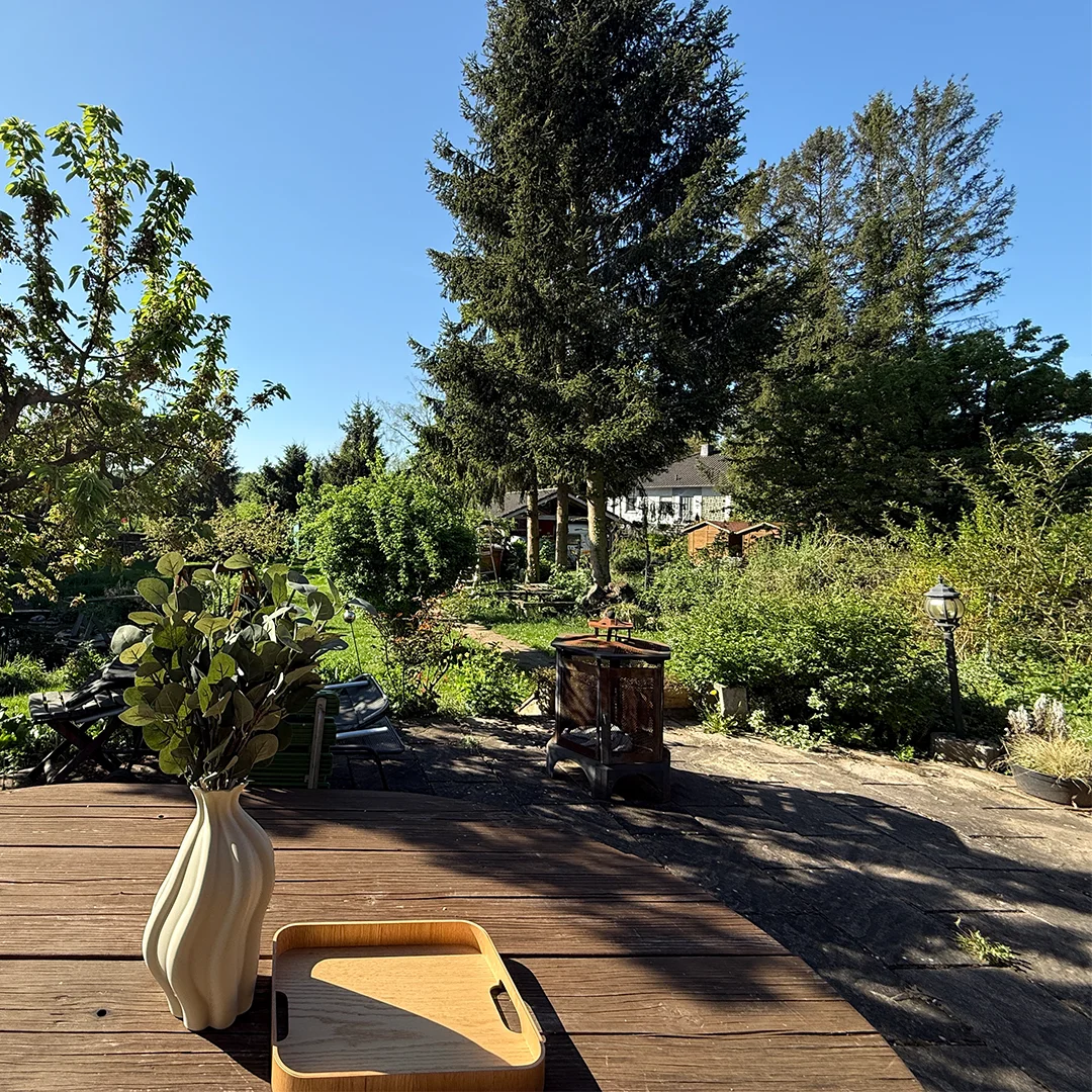 Holzhaus Mainz Marienborn An der Kirschhecke Gartenblick Holzterrasse mit Holzboden, angrenzendem Garten mit hoher Bepflanzung, großen Bäumen und natürlichem Tageslicht.