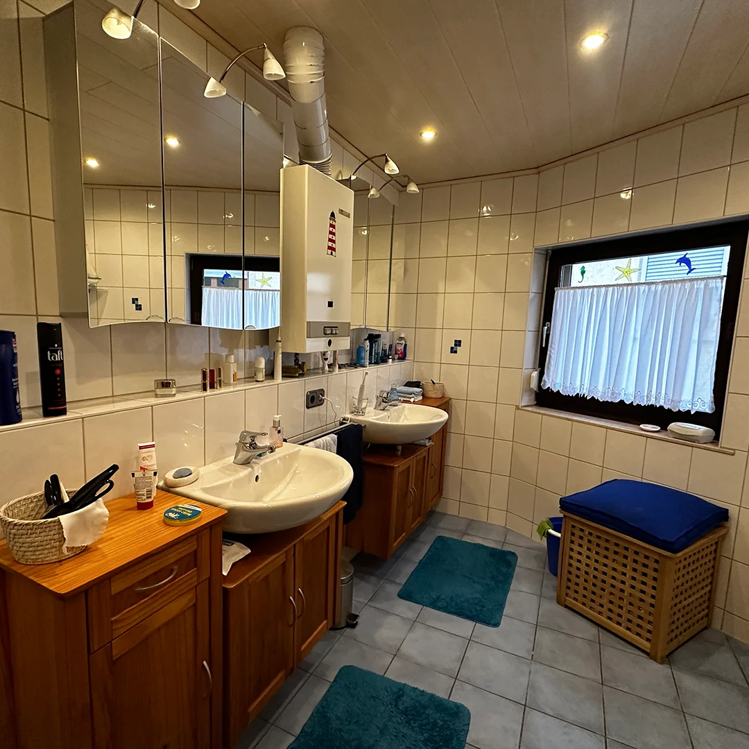 Mehrfamilienhaus Ingelheim Bahnhofstraße Badezimmer Raum mit gefliesten Wänden, zwei Waschbecken mit Unterschränken, Spiegel, Fenster und Beleuchtung an der Decke.