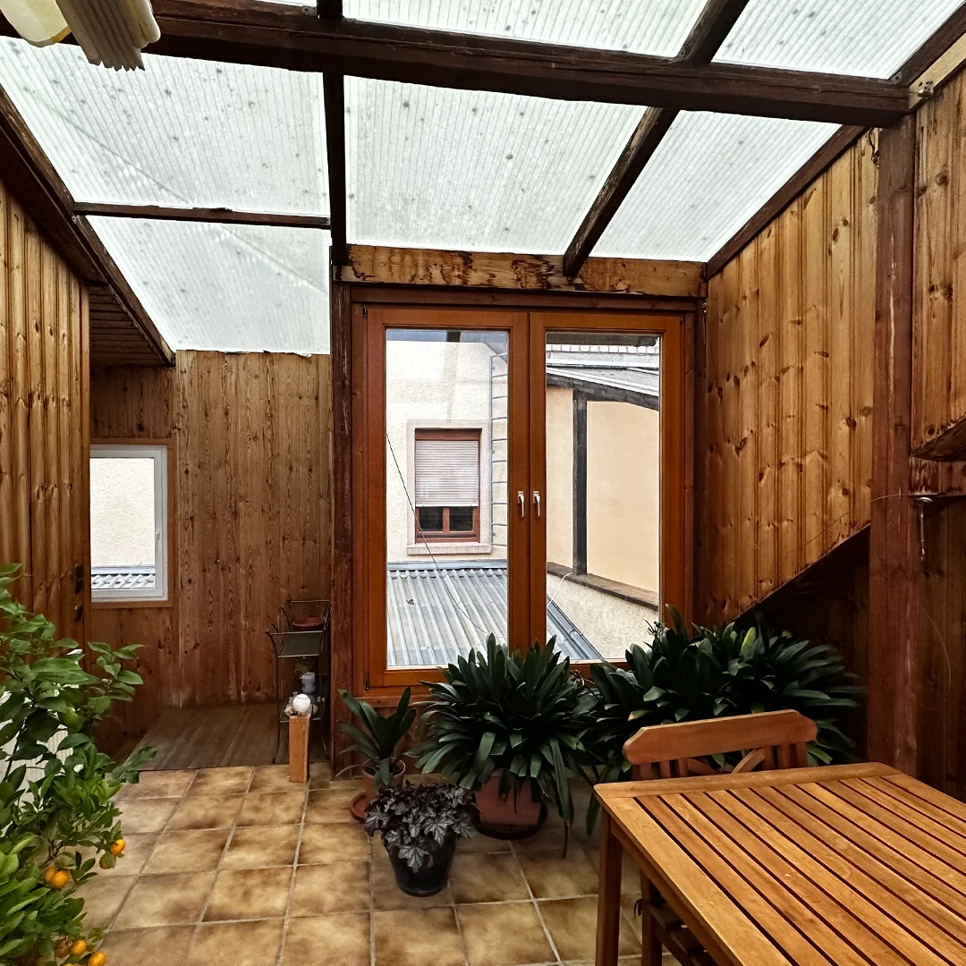 Mehrfamilienhaus Ingelheim Bahnhofstraße Terrasse Raum mit Holzverkleidung, transparentem Dach, gefliestem Boden, großem Fenster, mehreren Pflanzen sowie Holztisch und Stühlen.