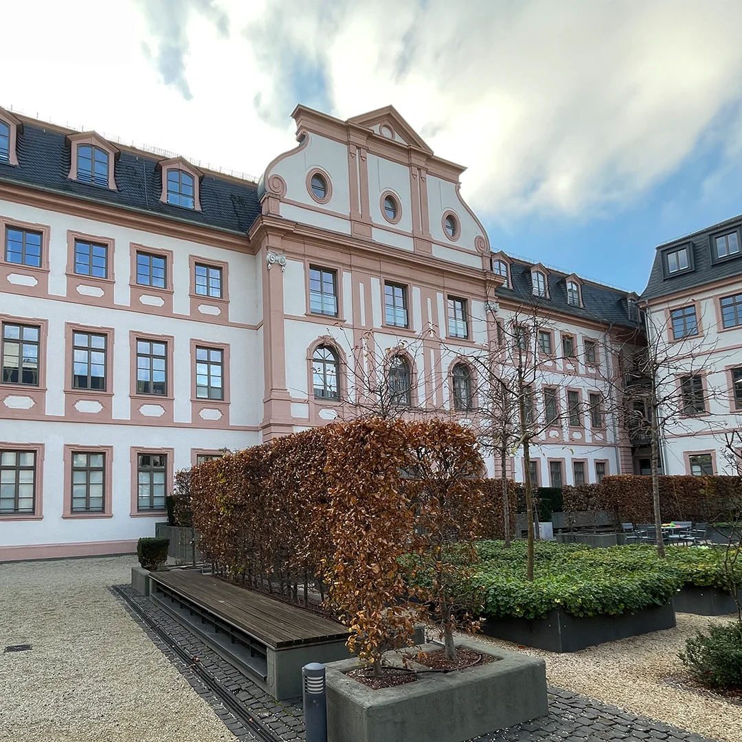 Wohnung Mainz Klarastraße Innenhof Gebäude mit gegliederter Fassade, symmetrischer Fensteranordnung, Dachgauben, gepflastertem Innenhof, Hochbeeten und natürlichem Tageslicht.