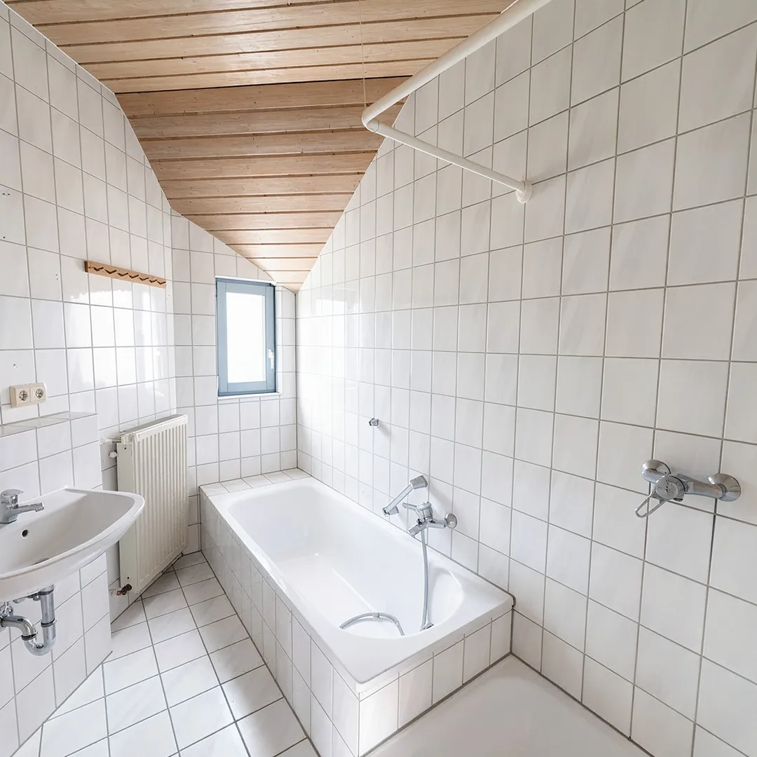 Helles Badezimmer mit Badewanne, Waschbecken, Toilette und weißen Fliesen.