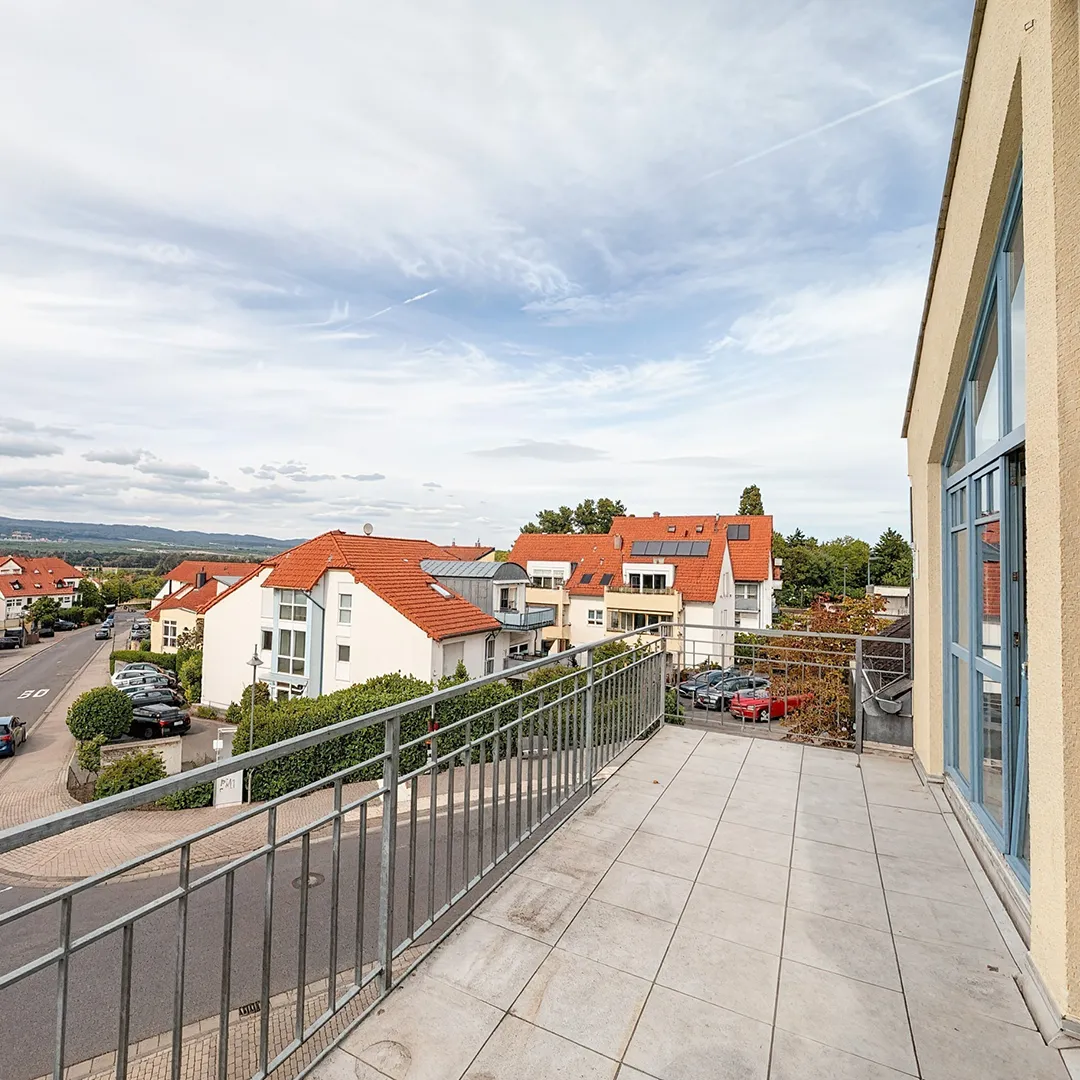 Aussicht vom Balkon auf Häuser, der Balkon hat graue Steinplatten und ein Metallgeländer