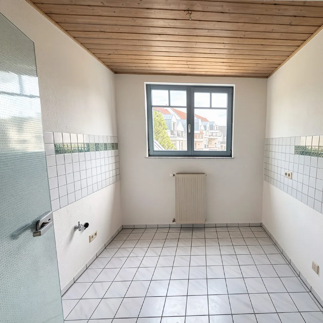 Küchenbereich mit hellen Fliesen und großem Fenster in der Mitte des Raumes