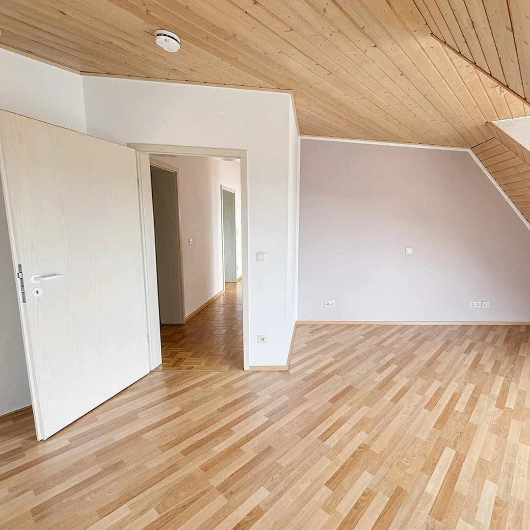 Helles Schlafzimmer mit Parkettboden, Dachschräge und großen Fenstern mit Blick auf die umliegende Landschaft.