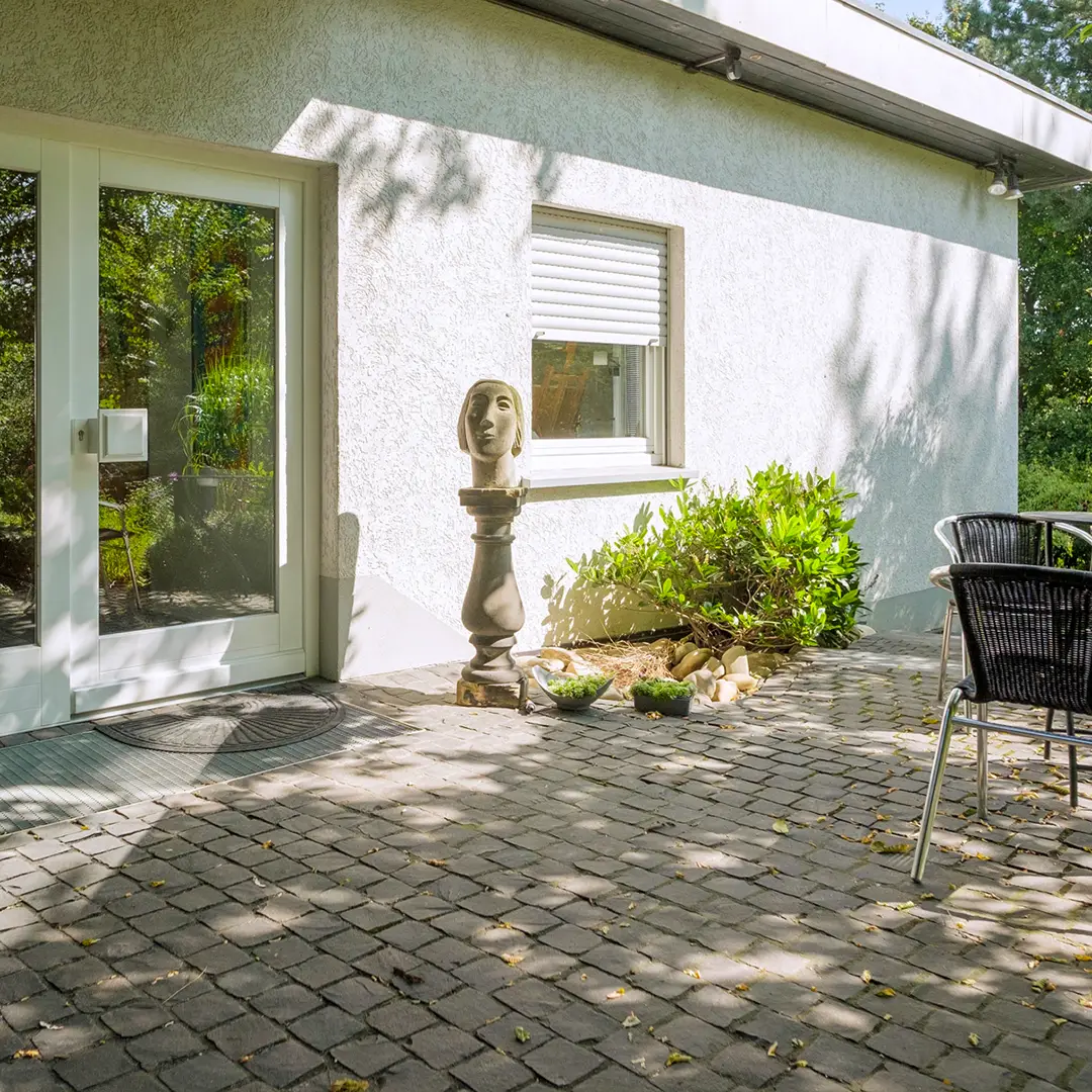 Überdachter Eingangsbereich eines Einfamilienhauses in Wackernheim mit gepflasterter Terrasse, Sitzbereich und bepflanztem Vorgarten