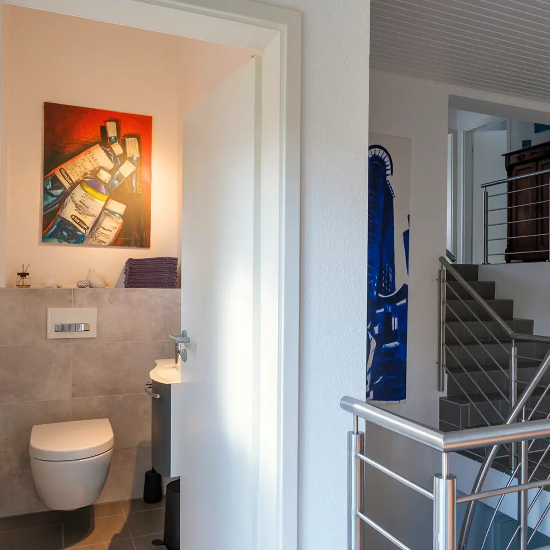 Modernes Gäste-WC mit wandhängendem WC und Waschbecken neben dem Treppenaufgang eines Einfamilienhauses in Wackernheim